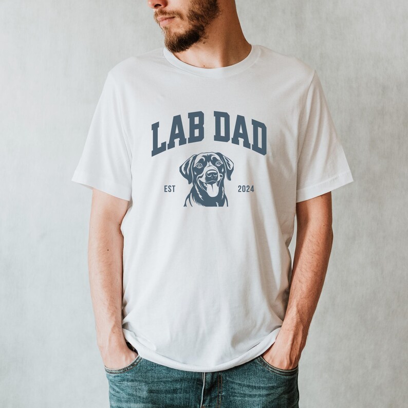 May include: White t-shirt with the text "Lab Dad" in blue, featuring a black Labrador Retriever silhouette and the text "Est 2024".