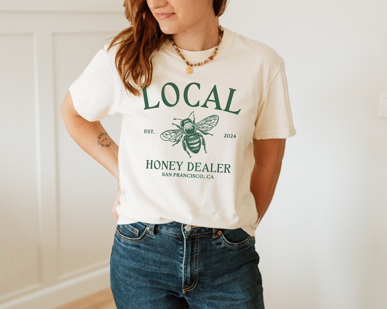 May include: A white t-shirt with a green graphic of a bee and the text "LOCAL EST. 2024 HONEY DEALER SAN FRANCISCO, CA"
