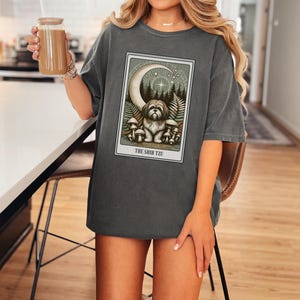 May include: A dark gray oversized t-shirt with a graphic print of a Shih Tzu dog surrounded by mushrooms and a crescent moon. The text "THE SHIH TZU" is printed below the image.