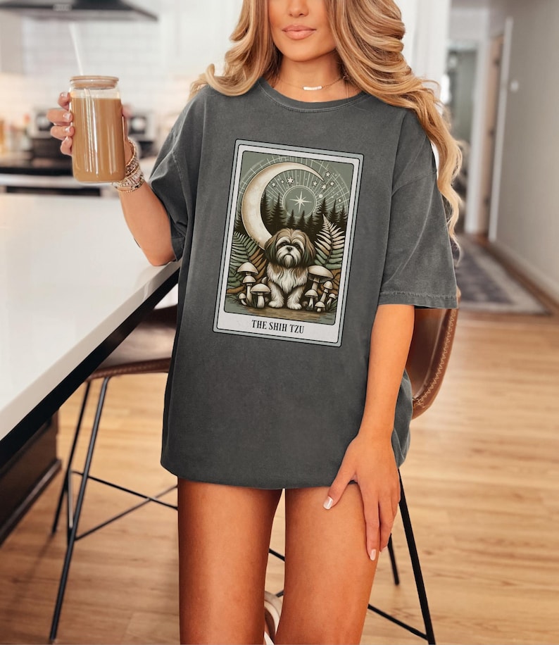 May include: A dark gray oversized t-shirt with a graphic print of a Shih Tzu dog surrounded by mushrooms and a crescent moon. The text "THE SHIH TZU" is printed below the image.