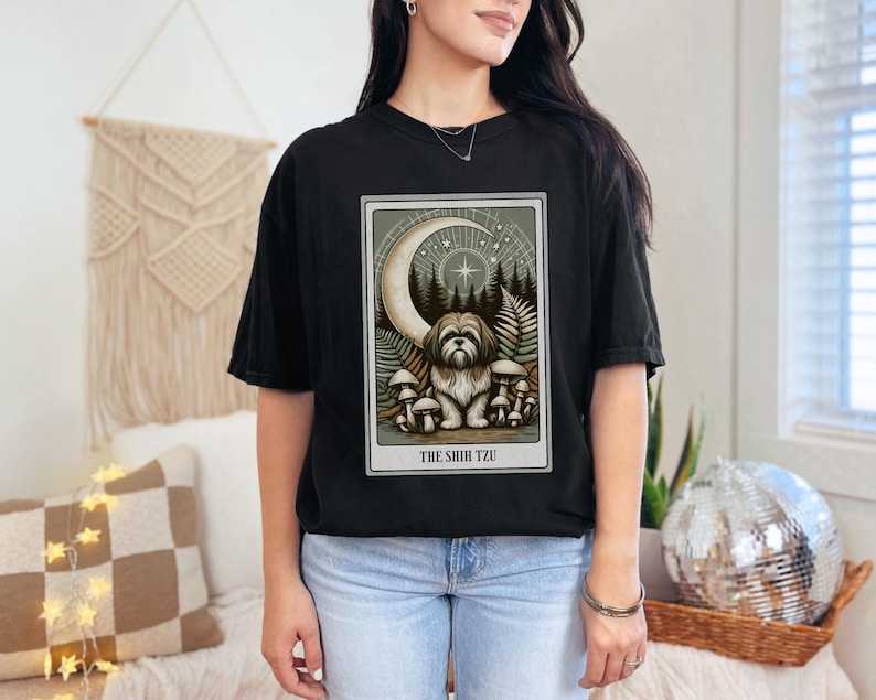May include: Black t-shirt with a graphic of a Shih Tzu dog sitting in a forest with a crescent moon and stars. The text "THE SHIH TZU" is below the image.