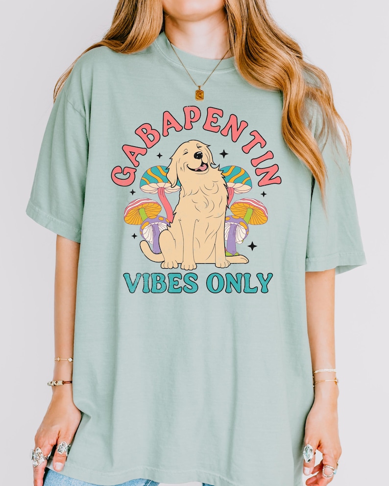 K&ouml;nnte beinhalten: Ein hellgr&uuml;nes T-Shirt mit einem Aufdruck eines Golden Retrievers, der vor drei Pilzen sitzt. Der Text "Gabapentin Vibes Only" ist auf dem T-Shirt aufgedruckt.