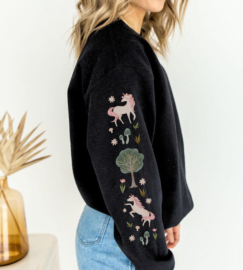 May include: Black sweatshirt with a unicorn, tree, and mushroom design on the sleeve. The design is in pink, green, and white.
