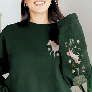 May include: A dark green sweatshirt with a white unicorn and floral design on the front and a white unicorn and floral design on the sleeve.