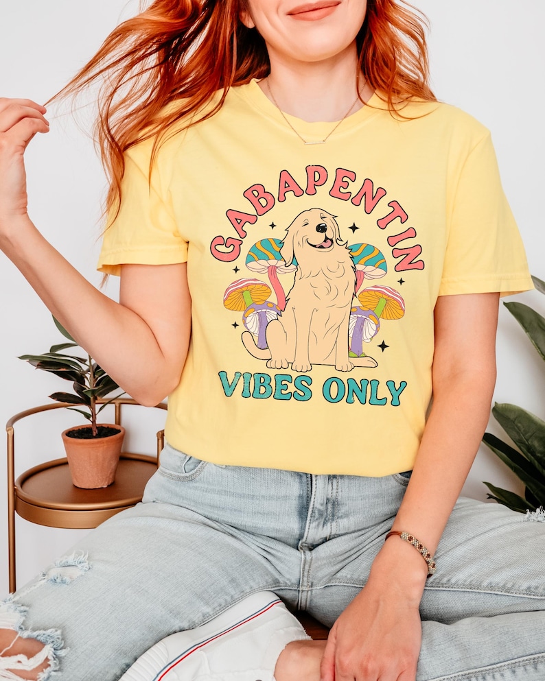 K&ouml;nnte beinhalten: Gelbes T-Shirt mit einem Grafikdruck eines Golden Retrievers, der vor Pilzen sitzt, mit dem Text "Gabapentin Vibes Only".
