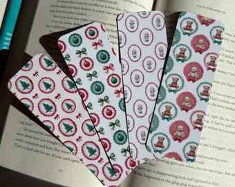 May include: Four decorative bookmarks with festive patterns. Designs include Christmas trees, ornaments, bows, and teddy bears in red, green, and white. The bookmarks are fanned out over an open book.