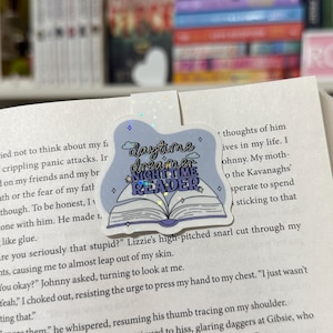 May include: A purple and white bookmark with a book illustration and the text "Daytime Dreamer, Nighttime Reader".