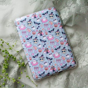 May include: A rectangular tablet case featuring a light blue background with a repeating pattern of summer and Halloween icons including ghosts in pink pool floats, smiling suns with sunglasses, bats, pumpkins, beach balls, flip-flops, and drinks.