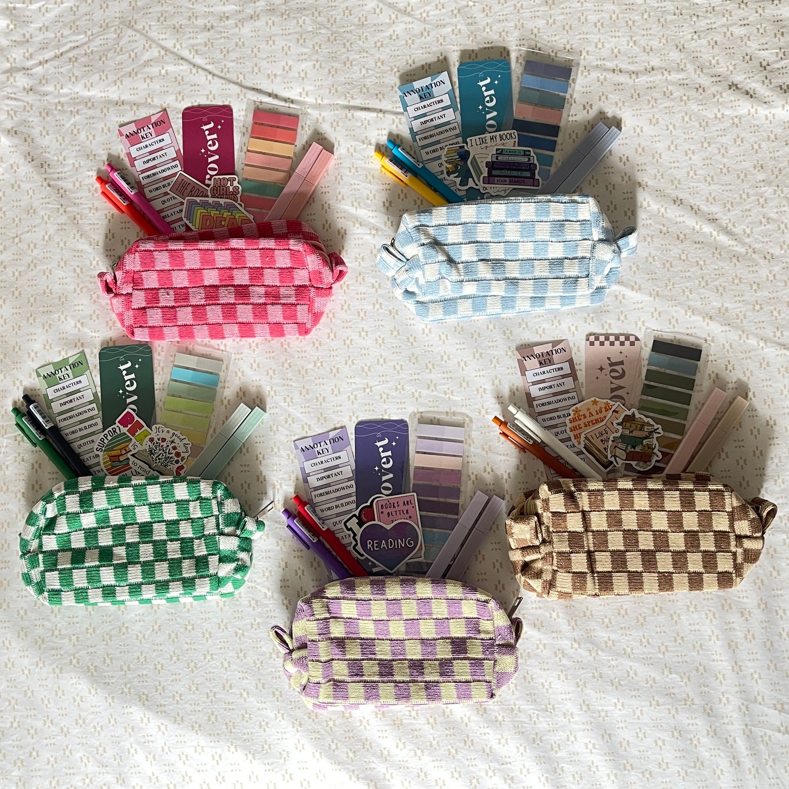 Five checkered pouches in pink, blue, brown, purple, and green laid out on a sheet with a variety of pens, tabs, and stickers sticking out of them.