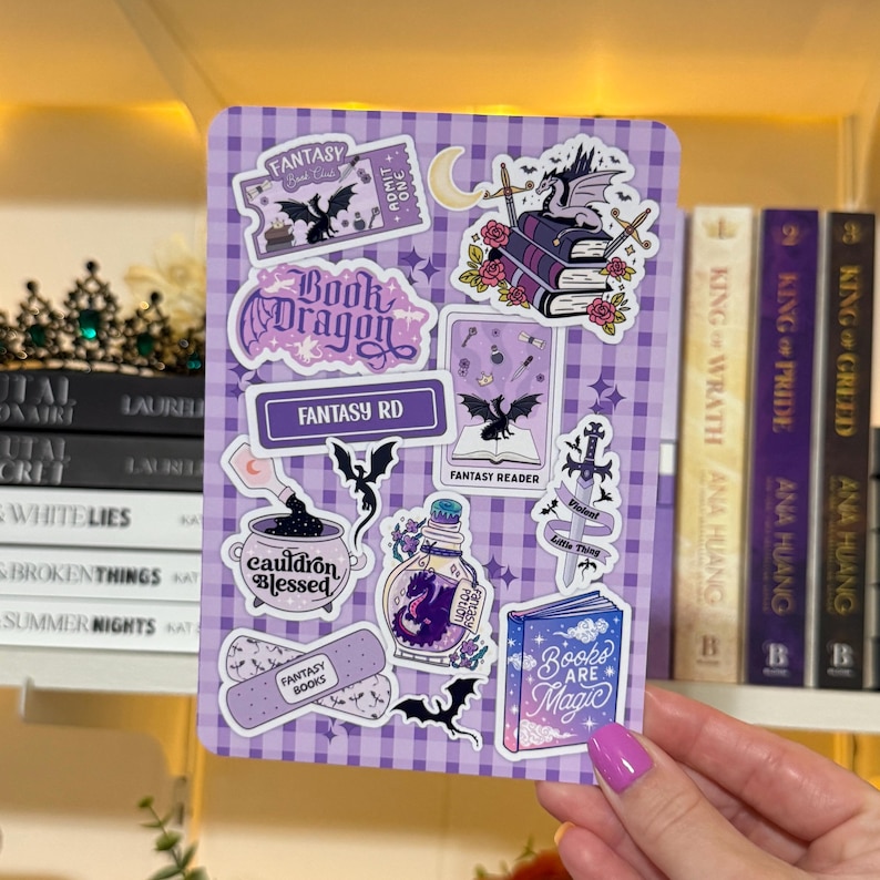 May include: A purple and white checkered sticker sheet with fantasy-themed illustrations. The sheet features stickers of dragons, books, potions, and the text "Fantasy RD" and "Books are Magic".