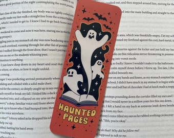 May include: A bookmark featuring a red and orange background with three white ghosts. The ghosts are flying over a closed book with the text "Haunted Pages" in white letters. The bookmark is decorated with white stars and black bats.