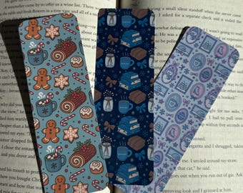 May include: Three decorative bookmarks with festive holiday patterns. One bookmark features gingerbread men, hot cocoa, and candy canes on a teal background. Another has books, bows, and mugs on a navy background. The third has frames and bows on a lavender background.