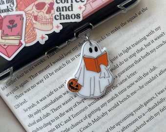 May include: A white ghost holding an orange book with a jack-o-lantern charm. The ghost is a Halloween-themed charm for a phone case. The text "coffee and chaos" is visible on a sticker in the background.