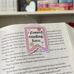 May include: A pink and white bookmark with the text "I stopped reading here" in a pink banner. The bookmark has a heart, stars, and flowers on it.
