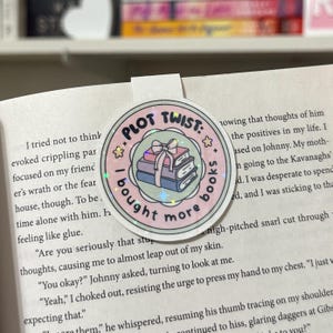 May include: A pink and green round sticker with glitter. The sticker has a stack of books with a bow on top and the text "PLOT TWIST: I bought more books".