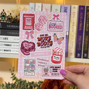 May include: A pink sticker sheet with various book-themed designs. Includes phrases like "Give Me More Books," "Emotional Support Book," and "Late Night Book Club." Features bows, dice, a butterfly, and a jar of jam.