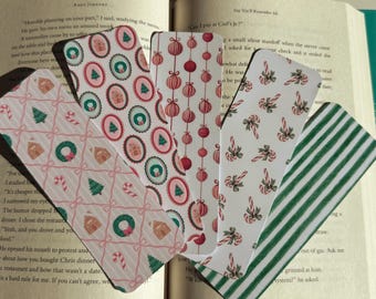 May include: A collection of Christmas-themed bookmarks with various patterns. Designs include gingerbread houses, Christmas trees, candy canes, ornaments, and green stripes. The bookmarks are displayed on an open book.