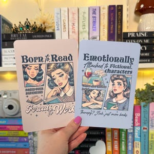 May include: Two cards with vintage-style illustrations and text. One card reads "Born to Read, Forced to Work" with a crying woman. The other says "Emotionally Attached to Fictional Characters." Both cards feature a retro comic book style.