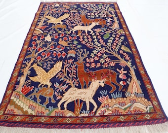 May include: A rectangular, hand-woven rug with a navy blue background. The rug features a detailed design of trees, deer, birds, and floral elements in shades of red, brown, beige, and white. The border is a mix of red, brown, and beige.