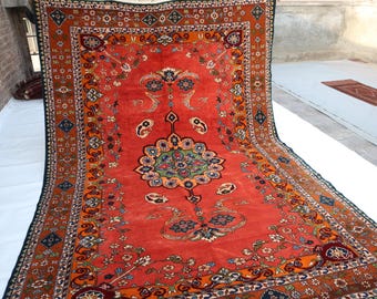 May include: A large, rectangular, red oriental rug with intricate floral and geometric patterns. The rug features a central medallion design with blue, green, and orange accents, surrounded by a detailed border.