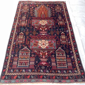 May include: A rectangular, hand-knotted rug with a dark blue background and intricate geometric patterns. The rug features a central floral motif in shades of cream, teal, and red, surrounded by stylized architectural elements and borders. The rug measures approximately 152 cm by 229 cm.
