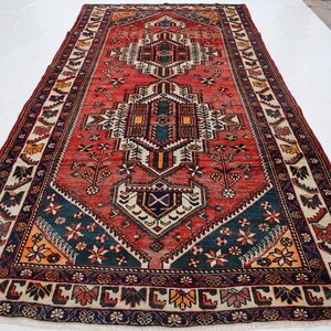 May include: A rectangular, hand-woven rug with a central geometric design in red, navy, and cream. The rug features intricate patterns and borders with floral and geometric motifs. The rug's dimensions are approximately 6 x 10 feet.