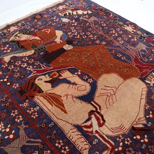 May include: A detailed, hand-woven rug with a deep blue background and intricate patterns. The rug features figures in shades of tan, brown, and red, with floral and geometric designs. The rug's border has a fringed edge.