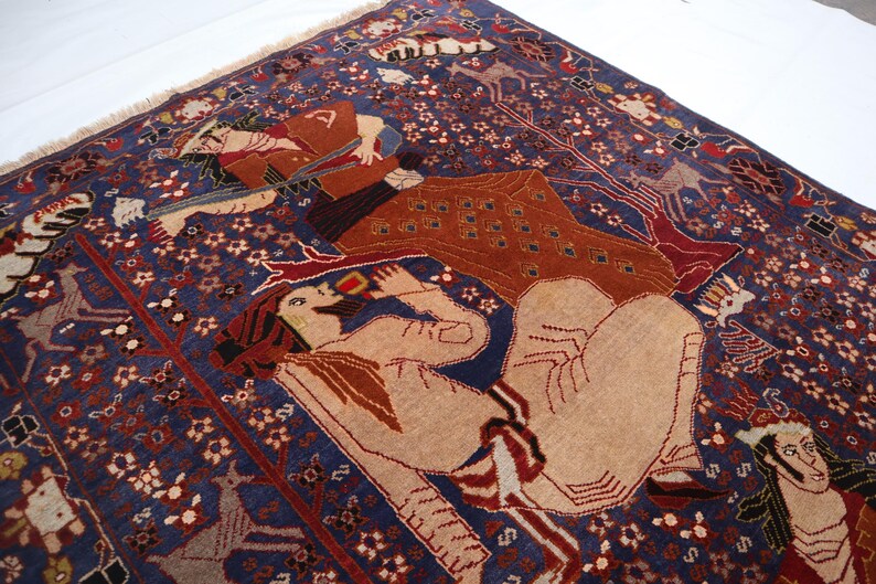 May include: A detailed, hand-woven rug with a deep blue background and intricate patterns. The rug features figures in shades of tan, brown, and red, with floral and geometric designs. The rug's border has a fringed edge.