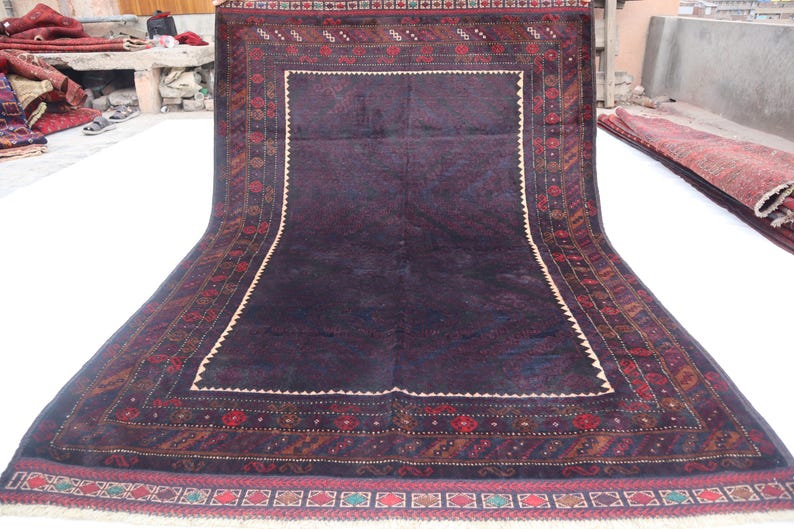 May include: A dark blue rug with a detailed, intricate pattern in shades of red, brown, and cream. The rug has a fringe border.