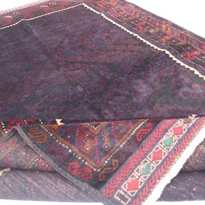 May include: A dark purple and red rug with intricate patterns. The rug is folded in half, revealing the underside, which is a lighter shade of purple.