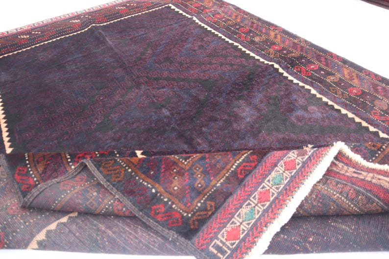 May include: A dark purple and red rug with intricate patterns. The rug is folded in half, revealing the underside, which is a lighter shade of purple.