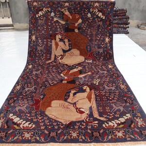 May include: A large, rectangular Persian rug with a deep blue background. The rug features a detailed design with figures, animals, and floral patterns in shades of brown, beige, and red. The rug is displayed on a white surface.