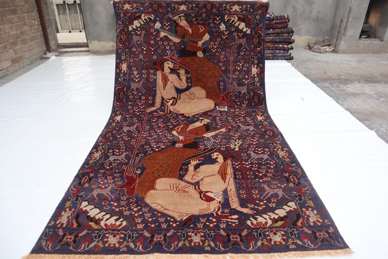 May include: A large, rectangular Persian rug with a deep blue background. The rug features a detailed design with figures, animals, and floral patterns in shades of brown, beige, and red. The rug is displayed on a white surface.