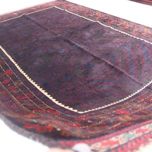 May include: A dark blue rug with a cream-colored border and intricate red, brown, and blue patterns. The rug has a traditional design and is made of wool.