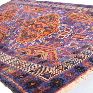 May include: A vintage rug with a blue background and intricate patterns in shades of orange, red, and green. The rug has a fringed edge and is woven with a variety of textures.
