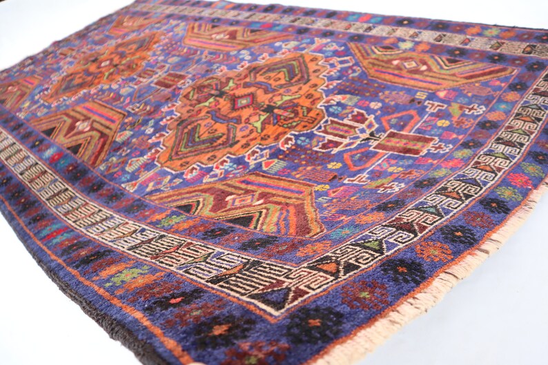 May include: A vintage rug with a blue background and intricate patterns in shades of orange, red, and green. The rug has a fringed edge and is woven with a variety of textures.