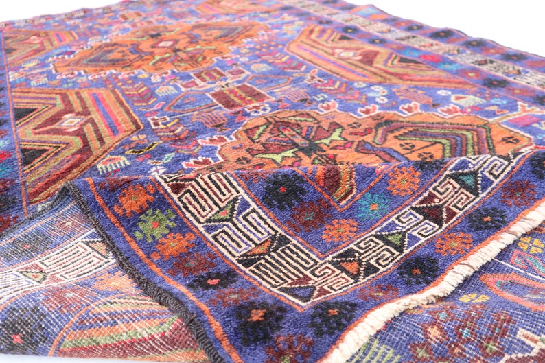 May include: A vintage Turkish rug with a blue background and intricate geometric patterns in shades of orange, red, green, and black. The rug has a fringe border and is folded in half.