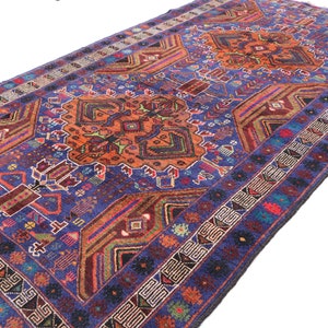 May include: A vintage Persian rug with a blue background and intricate geometric patterns in shades of orange, red, green, and blue. The rug has a fringe border.