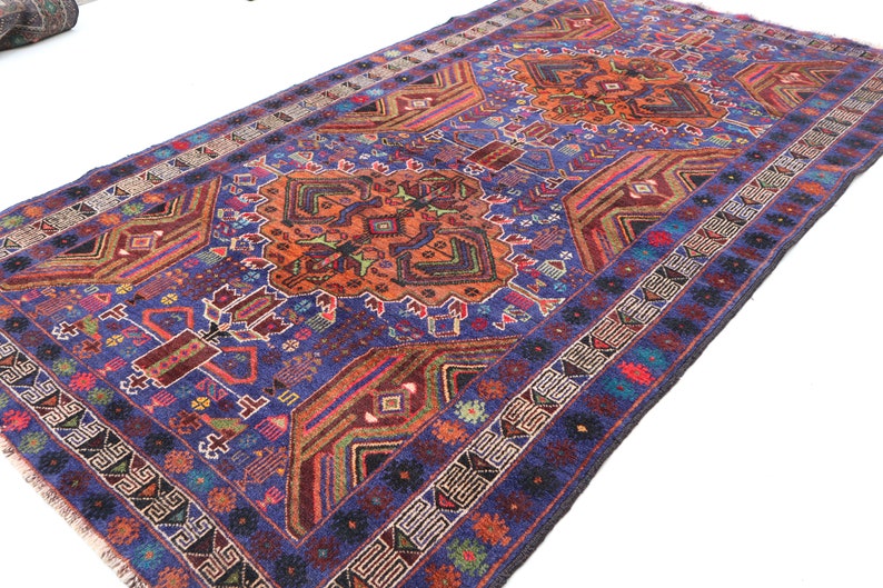 May include: A vintage Persian rug with a blue background and intricate geometric patterns in shades of orange, red, green, and blue. The rug has a fringe border.