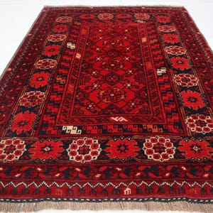 Pode incluir: Um tapete vermelho e preto com um medalhão central e desenhos intrincados na borda. O tapete tem franjas em todos os lados.