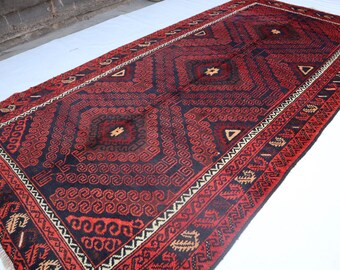 Op de afbeelding: Een rood en zwart tapijt met een geometrisch patroon. Het tapijt heeft een franje rand en is gemaakt van wol.