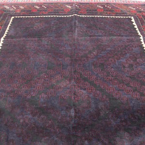 May include: A dark purple rug with a detailed geometric pattern in a lighter shade of purple. The rug has a white border with a red and black patterned trim.