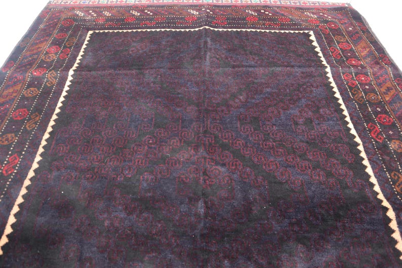 May include: A dark purple rug with a detailed geometric pattern in a lighter shade of purple. The rug has a white border with a red and black patterned trim.