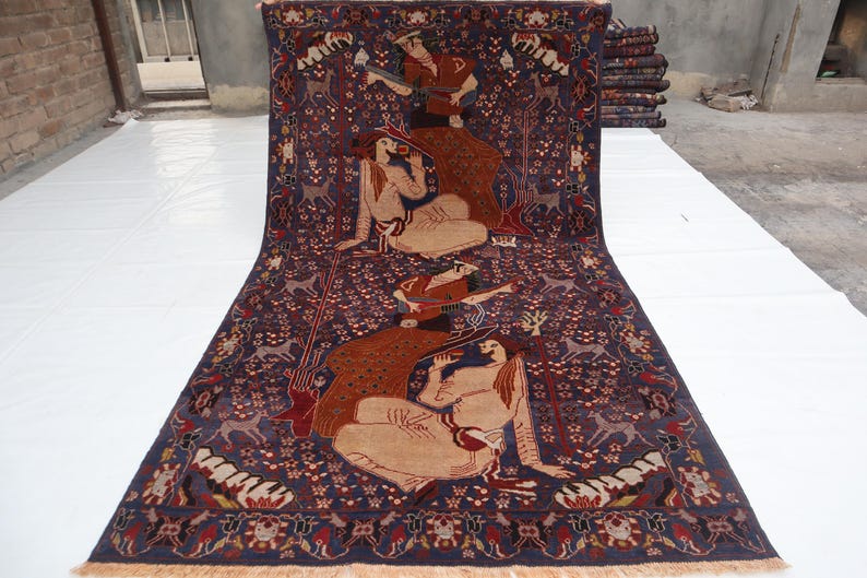 May include: A large, rectangular rug with a dark blue background and intricate patterns. The rug features figures, animals, and floral motifs in shades of brown, red, and beige. The rug has a fringed edge.