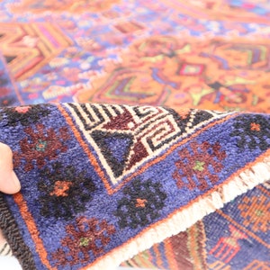 May include: A close-up of a blue and orange rug with intricate geometric patterns. The rug has a fringe border and is folded in half.