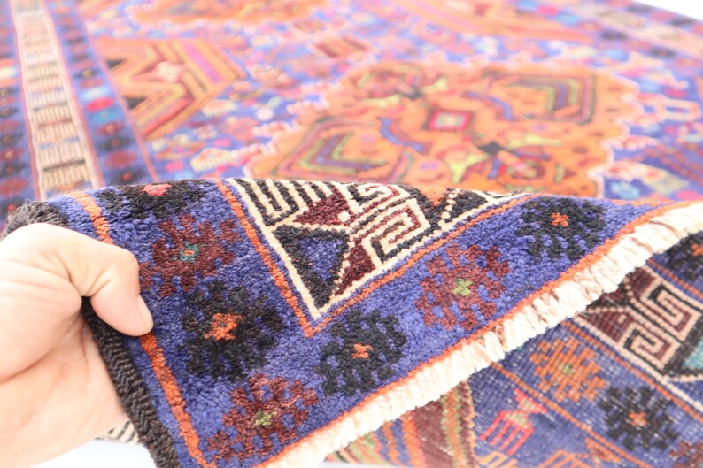 May include: A close-up of a blue and orange rug with intricate geometric patterns. The rug has a fringe border and is folded in half.