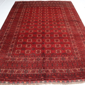 May include: A large, rectangular red rug with an intricate geometric pattern. The rug features a repeating design of squares and floral motifs in shades of red, brown, and beige. The rug has a fringed edge and is suitable for a living room or bedroom.