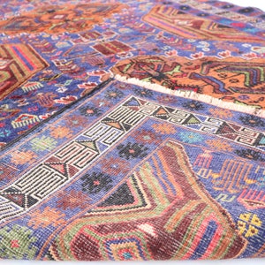 May include: A vintage rug with a blue background and intricate geometric patterns in shades of red, orange, green, and white. The rug has a fringed edge.