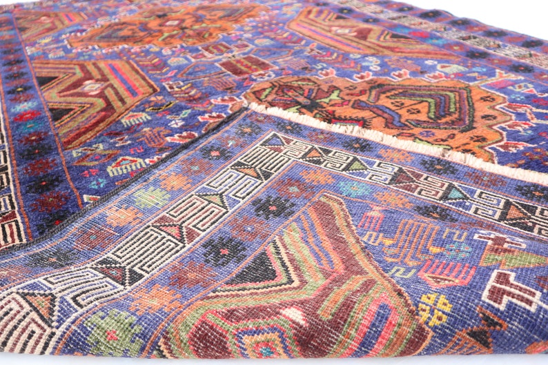 May include: A vintage rug with a blue background and intricate geometric patterns in shades of red, orange, green, and white. The rug has a fringed edge.