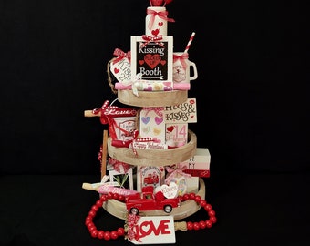 May include: A tiered tray decorated for Valentine's Day with red and white hearts, a red truck, and signs that say "Kissing Booth", "Hugs & Kisses", and "Love".